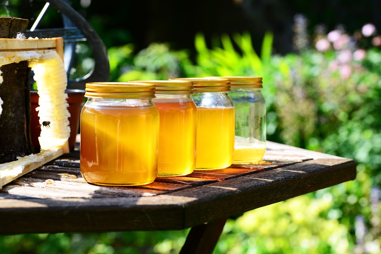 Picture of jars of honey on a table with flowers behind.